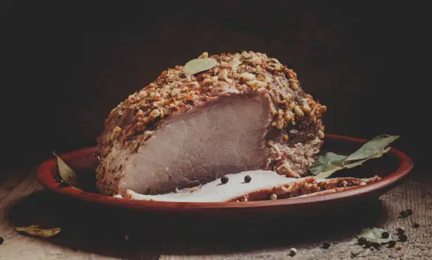 Delicious baked ham pork on a clay tray on the old wooden background, selective focus and toned image