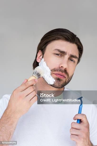 Portrait Of Man With Brush And Razor In Hands Putting Shaving Foam On Face On Grey Backdrop Stock Photo - Download Image Now