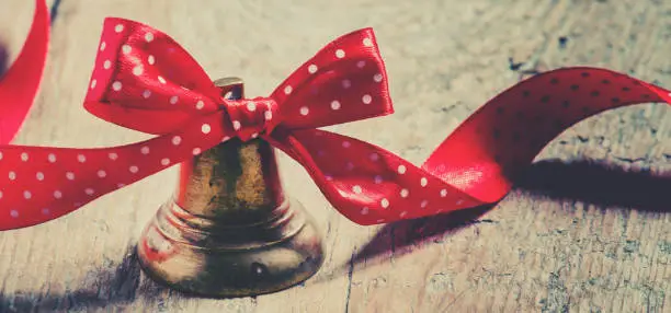 Photo of Jingle bells with a red ribbon with polka dots on old wooden background, stained toned image, selective focus and toned image