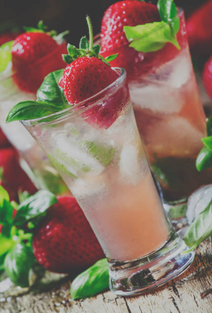 istock Alcoholic cocktail feeling with Cachaca, cranberry drink, strawberries, lime juice, green basil, and ice cubes, vintage wooden background, selective focus and toned image 1015512886