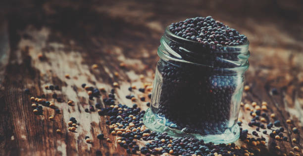 Black mustard seeds in a glass jar on the old wooden background, selective focus and toned image Black mustard seeds in a glass jar on the old wooden background, selective focus and toned image dijonnaise stock pictures, royalty-free photos & images