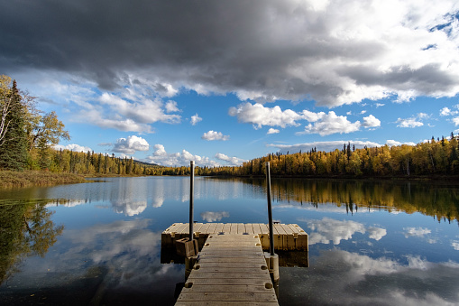 Pier on the Talkeetna lakes, open lake, autumn trees and reflection of clouds.