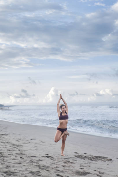 istock attractive young woman practicing yoga in tree pose (Vrksasana) on seashore 1015534252