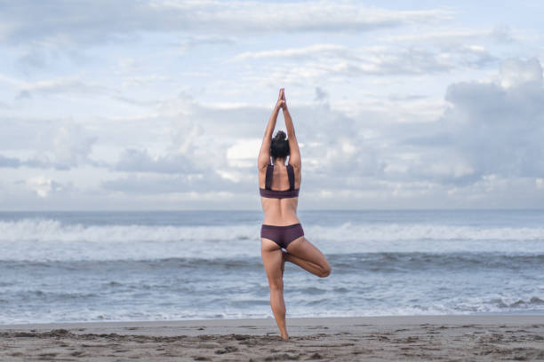 istock rear view of woman practicing yoga in tree pose (Vrksasana) on seashore 1015534254