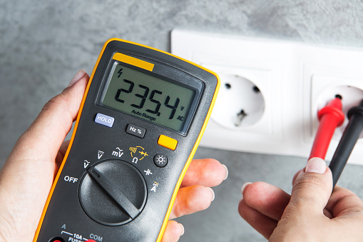 Woman checking voltage in power socket with tester close-up. Housewife hands with multimeter.