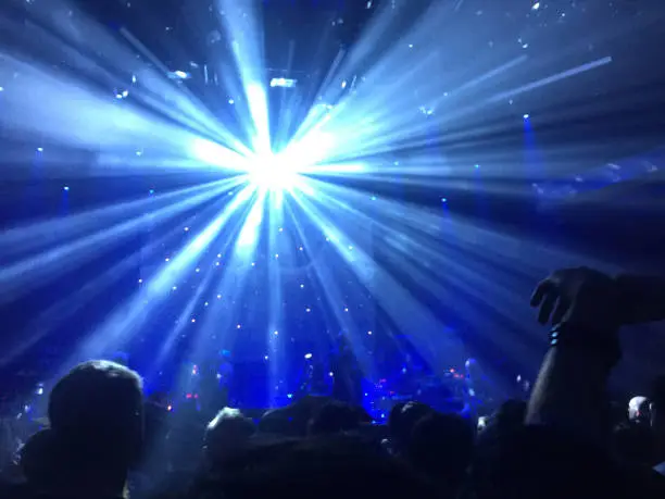 a dark concert hall filled with people and a bright shinning disco ball in the background above the silhouette of people