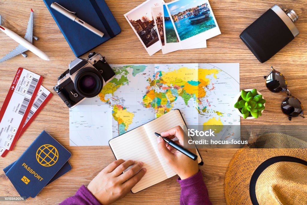 Making check list for travel Woman making a list for her travel, on a wooden desktop with travel accessories. Travel Stock Photo