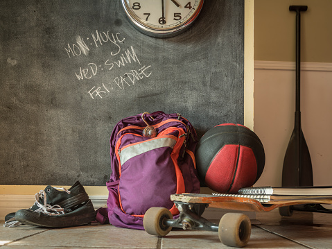 Everyday teenage belongings on the floor of the home interior. Paddle, back pack, basket ball and sport shoes against the wall with black board finish.