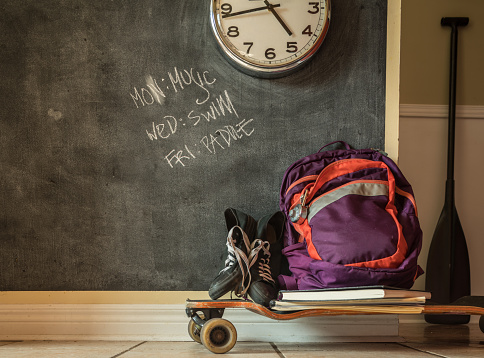 Everyday teenage belongings on the floor of the home interior. Paddle, back pack and sport shoes against the wall with black board finish.