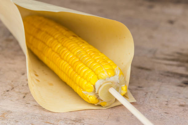 The grilled corn on a wooden stick in a paper bag on the table