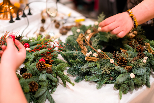 Taller tejido de la guirnalda de Navidad. Manos de mujer decoración corona de vacaciones hecho de ramas de abeto, conos y varias decoraciones orgánicas sobre la mesa photo