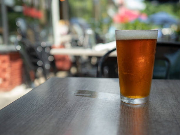 ледяное янтарное пиво, сидящее в пинте стакана на столе снаружи с мокрым кольцом чашки - amber beer стоковые фото и изображения