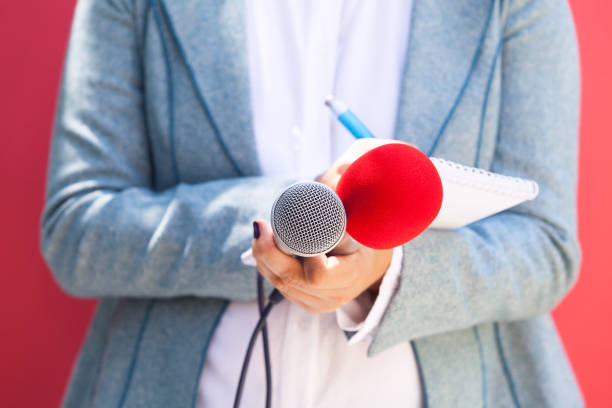 istock Female journalist at news conference, writing notes, holding microphone 1015588956