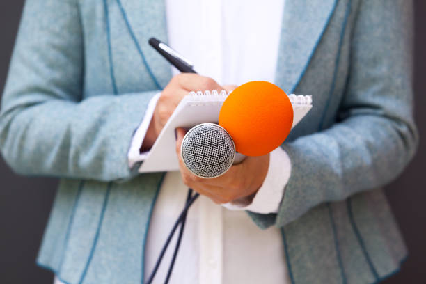 istock Female reporter at press conference, writing notes, holding microphone 1015589360