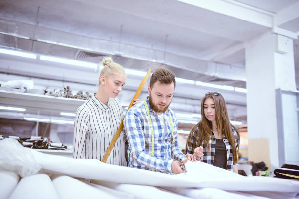 istock Chief Tailor Showing Apprentices How To Cut Cotton Fabric 1015595010