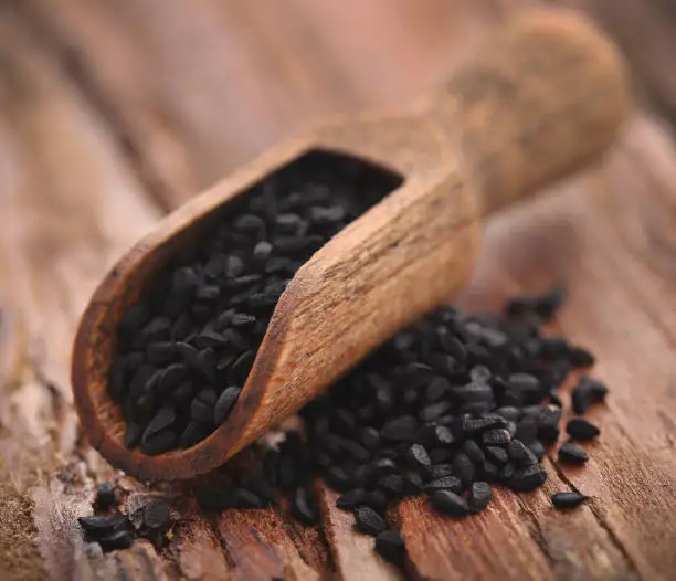 Nigella seeds in wooden scoop on timber surface