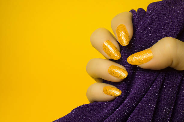 yellow glittered nails manicure Female hand with glittered yellow nails is holding purple textile on yellow background, manicure and nail care concept. yellow nail polish stock pictures, royalty-free photos & images