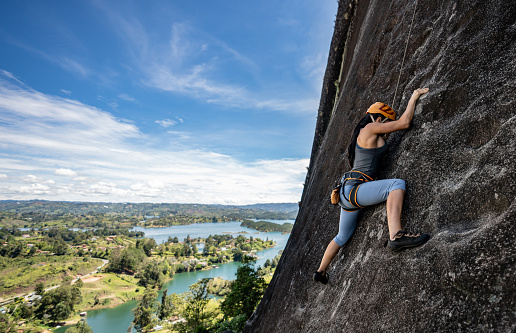 Strong woman rock climbing at Guatape in Colombia wearing a helmet and using ropes - adventure concepts