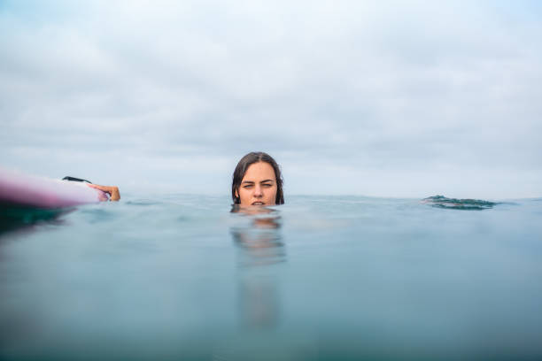 istock young woman swimming with surfboard on cloudy day 1015621230