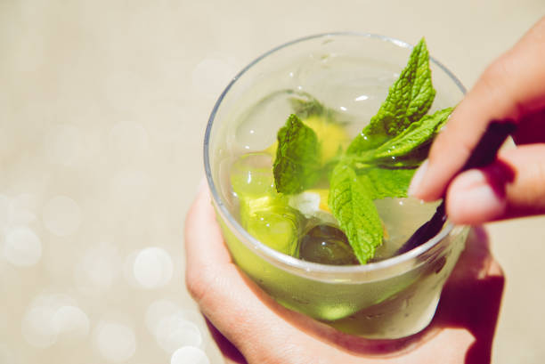 Female hand holding decorated mojito cocktail at the beach