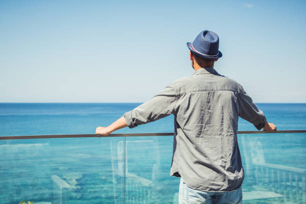 Young man standing on the balcony, looking into the distant horizon, enjoying the view