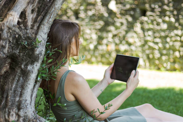 istock woman reading tablet and enjoy rest in a park under tree 1015650012