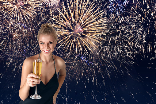 Young woman celebrating party with glass of champagne in her hands in front of fireworks