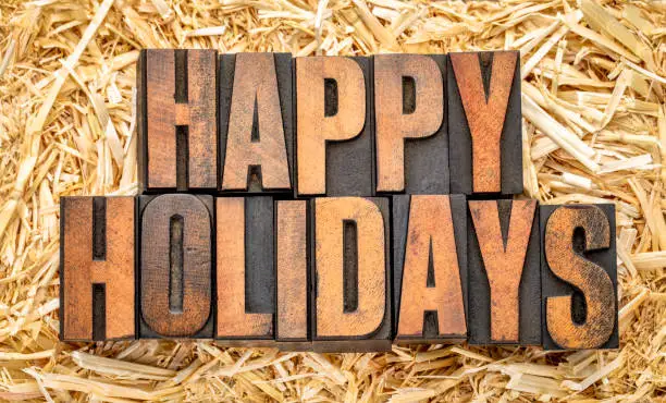 Happy Holidays banner or greeting card in vintage letterpress printing blocks against a straw bale