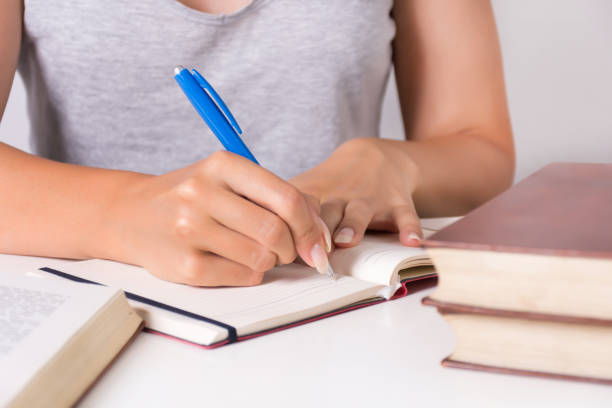 istock Young girl student writes in notebook with blue pen and full desk with book 1015708434