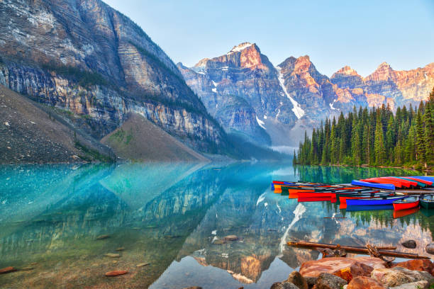 Sunrise Over the Canadian Rockies at Moraine Lake in Canada Sunrise over the Valley of the Ten Peaks with canoes on the glacier-fed, turquoise colored Moraine Lake in the Canadian Rockies. moraine lake stock pictures, royalty-free photos & images