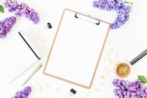 istock Workplace composition with clipboard, diary,, branches of lilac flowers and accessories on white background. Flat lay, top view. 1015746236