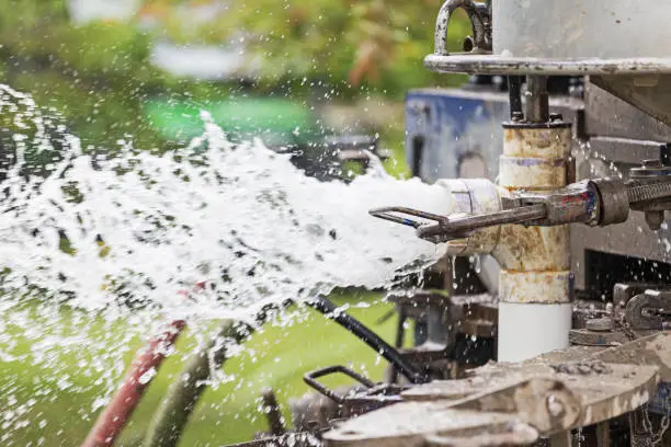 Close-up image of the process and equipment of drilling a new residential water well.  This image shows water forcefully spraying out of the new pcv water pipe.