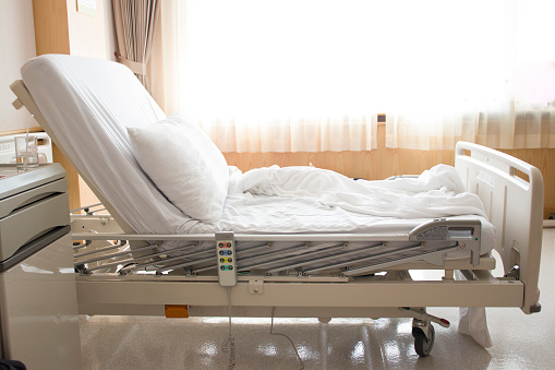 Stock photo showing close-up view of a medical recovery room with an adjustable gurney, which features clean white sheets, adjustable foot controls and wheels, so that the patient can be easily transported into surgery.