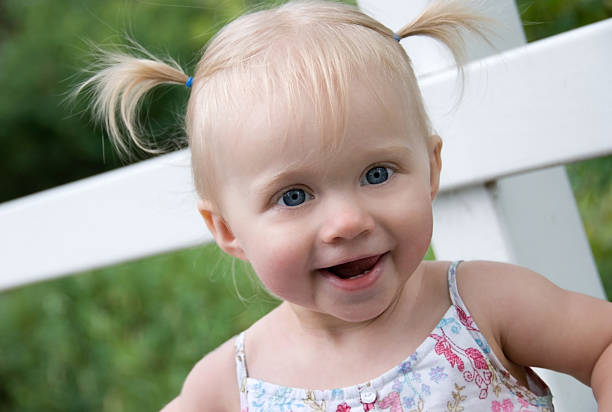 Lovely toddler girl sitting on bench in the park while looking at camera