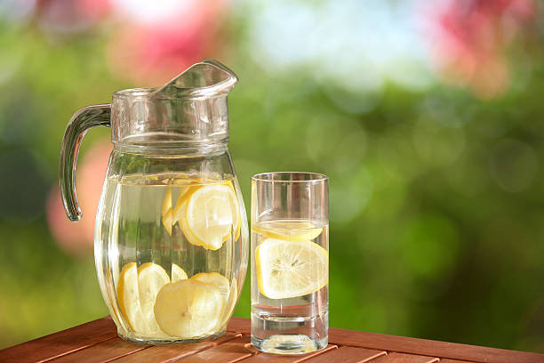 a glass and pitcher of fresh lemonade over table in garden.