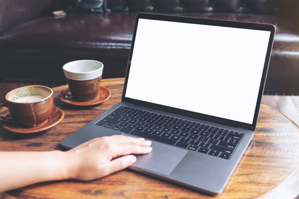 istock Mockup image of a hand using and typing on laptop with blank white screen and coffee cup on table in modern cafe 1015836456