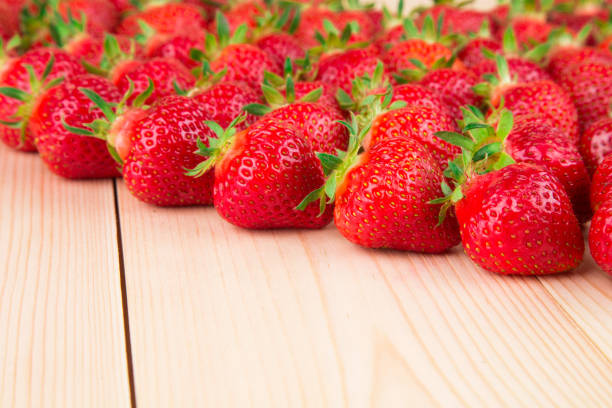 Rows of fresh strawberries. It is located in the wooden background. Close-up.