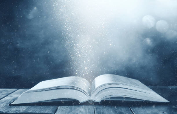 istock image of open antique book on wooden table with glitter background 1015855272