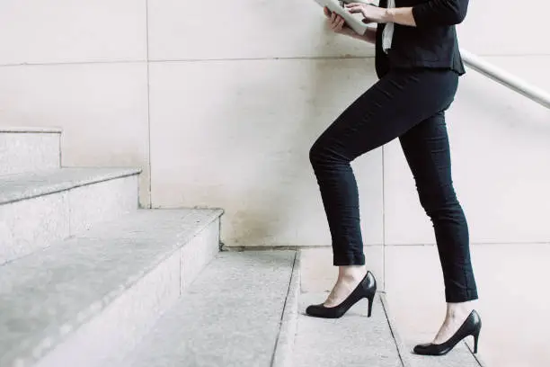 Portrait of young Caucasian businesswoman wearing high-heeled shoes walking upstairs and using digital tablet. Business concept