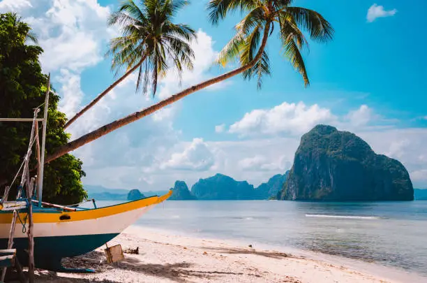 Banca boat on shore under palm trees.Tropical island scenic landscape. El-Nido, Palawan, Philippines, Southeast Asia