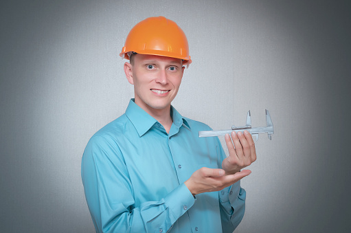 Happy builder worker measures something using a caliper in his hands isolated on gray background.
