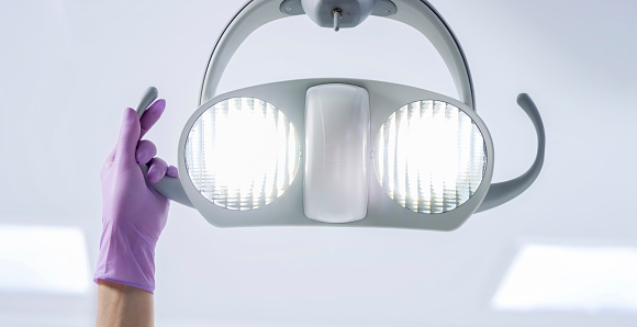 Female hand in violet glove moving dental light.