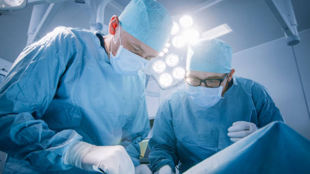 low angle shot in operating room of two surgeons during the surgery procedure bending over patient with instruments. professional doctors in modern hospital - cirurgia imagens e fotografias de stock