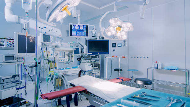 establishing shot of technologically advanced operating room with no people, ready for surgery. real modern operating theater with working equipment,  lights and computers ready for surgeons and a patients. - equipamento médico imagens e fotografias de stock