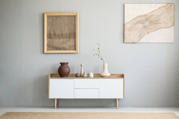 front view of burlap artworks on a light gray wall above a wooden cupboard with decorations in real photo of a living room interior with a place for your armchair - sideboard imagens e fotografias de stock