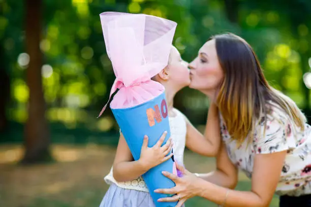 Happy little kid girl and mother with big traditional school gift cone in Germany. schoolkid on first day of elementary class. Back to school concept. Healthy child and woman kissing and hugging