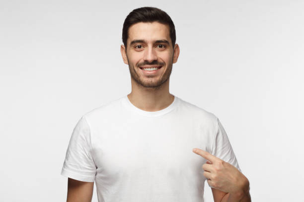 istock Smiling nice man pointing at his blank white t-shirt with index finger, copy space for your advertising, isolated on grey background 1015970262