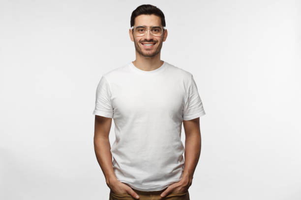 istock Handsome man in white tshirt and trasparent eyeglasses isolated on grey background, smiling, standing in hands in pockets pose 1015970324