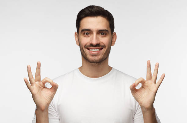 istock Good looking man isolated on grey background smiling, and showing okay sign with two hands, sharing positive experience addressing audience with advice 1015970528