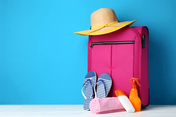 istock Pink suitcase with flip-flops, hat and sunscreen bottles on wooden table 1015970636